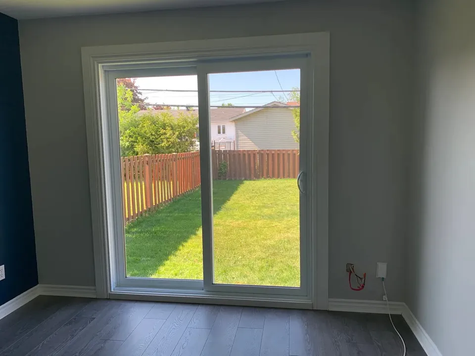 Interior view of a white sliding glazed door facing a fenced yard.