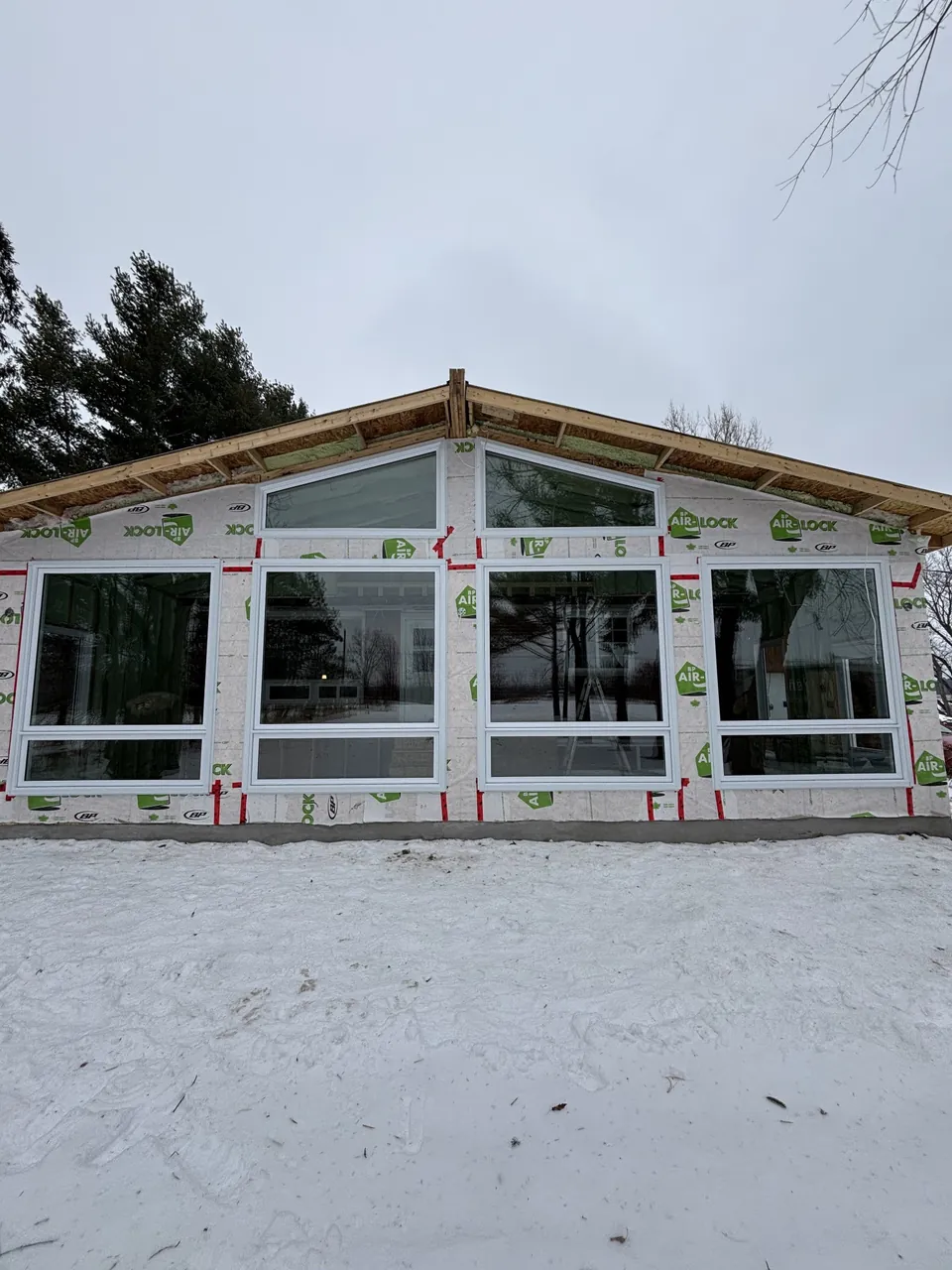 Façade under construction with large white windows and two trapezoidal windows beneath the roof.