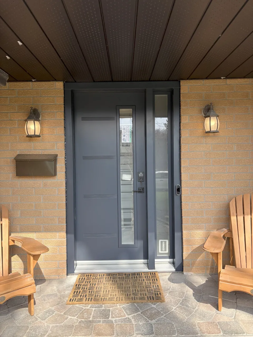 Dark entrance door with narrow vertical glazing and a sidelight beneath a porch.