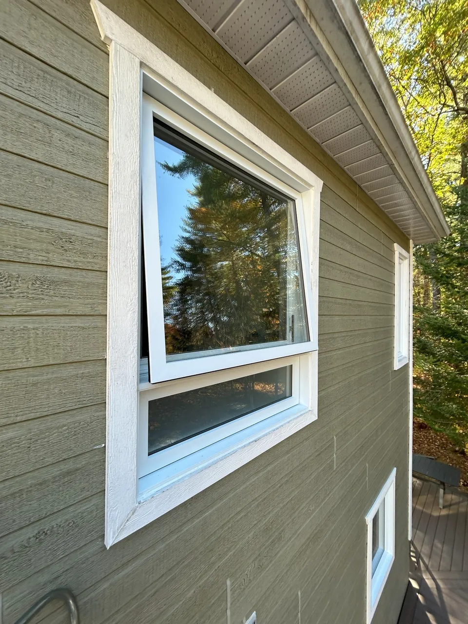 White awning window opened outward in a wall with horizontal siding.