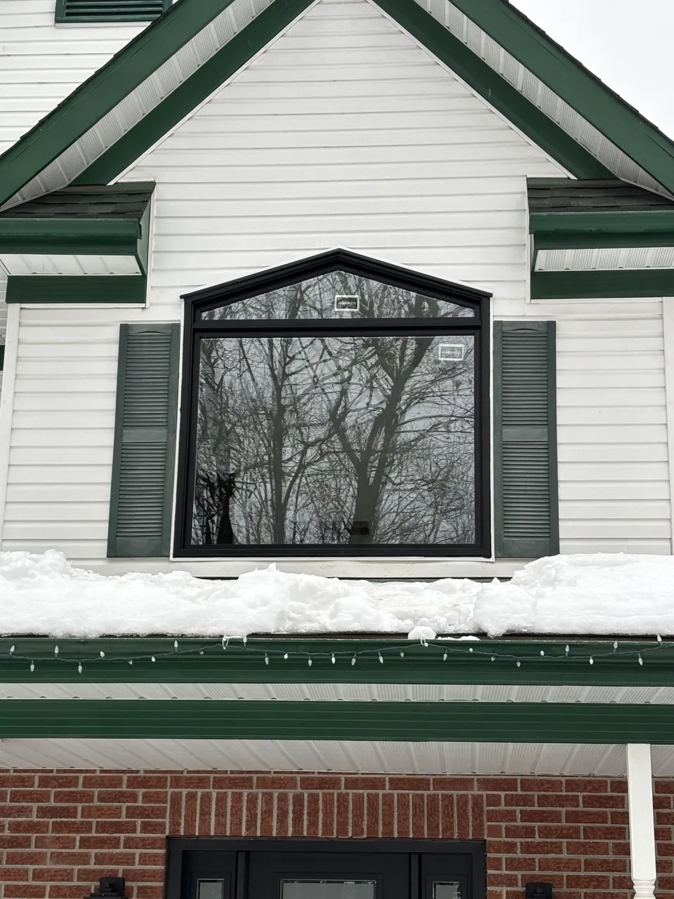 Fenêtre noire avec une partie supérieure en pointe, dans une façade blanche à bordures vertes.