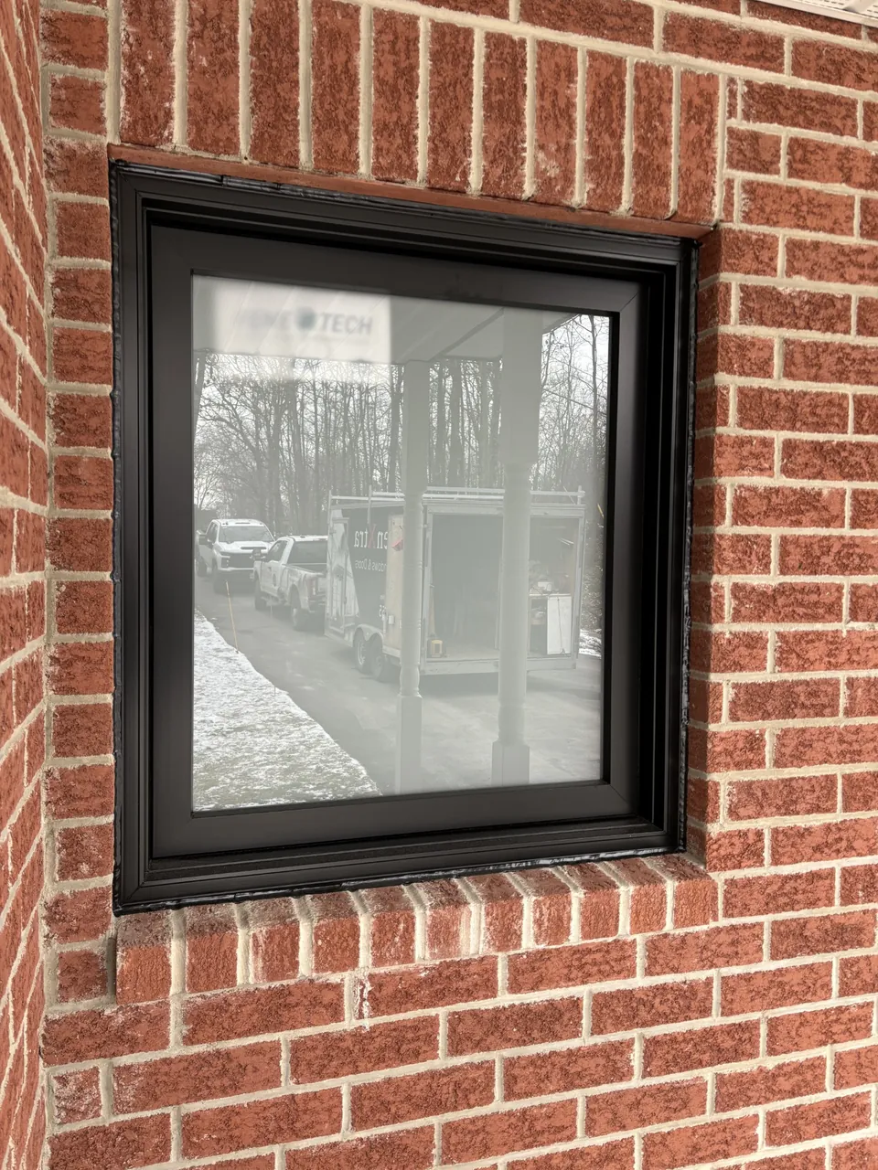 Black-framed window in a brick wall, with reflections in the glass.