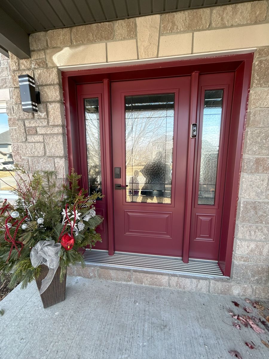 Glazed burgundy door and sidelights in a stone exterior, with a planted arrangement on the left.