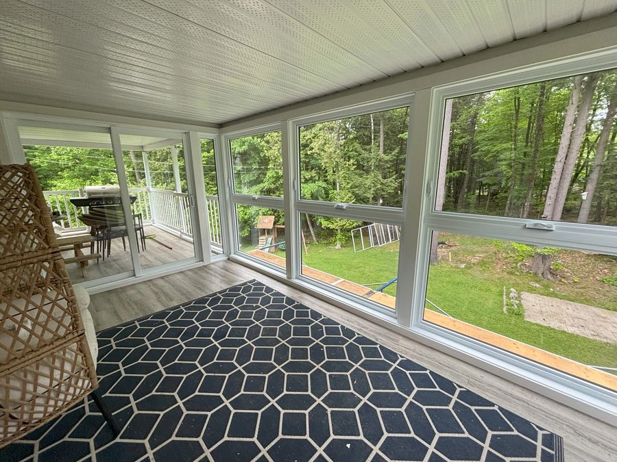 White-framed glazed room with a sliding door, patterned rug and a view of trees.