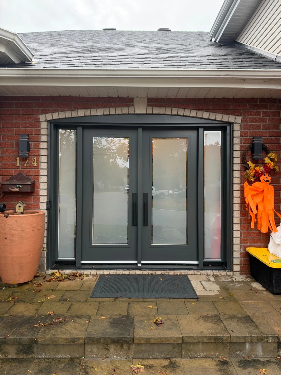 Dark grey double entrance doors with two large glass panels and glazed sidelights in a brick façade.
