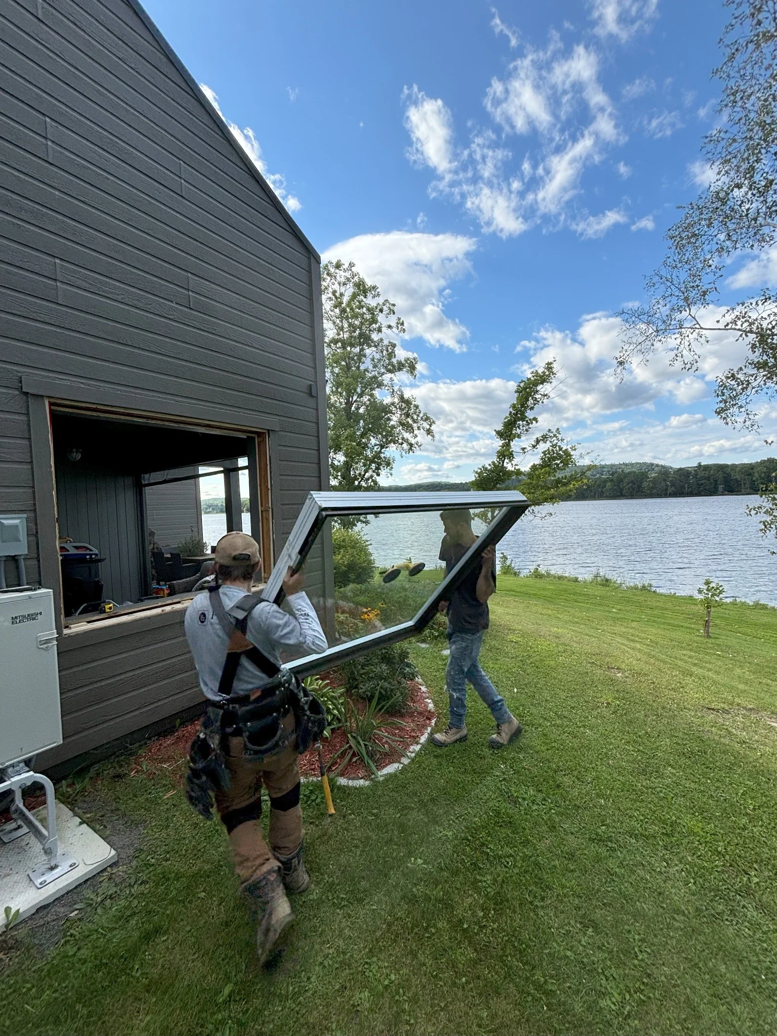 Two FenXtra installers carry a window outside a lakeside home.