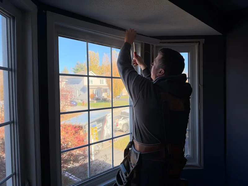 Un installateur travaille sur la moulure supérieure d’une fenêtre, à l’intérieur de la maison.