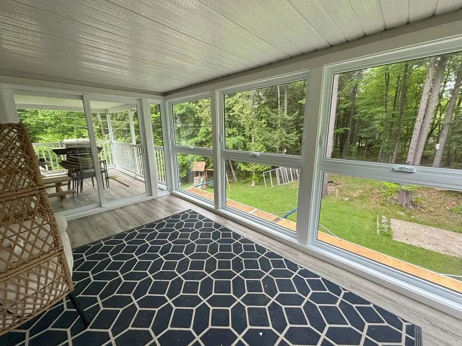 White-framed glazed room with a sliding door, patterned rug and a view of trees.