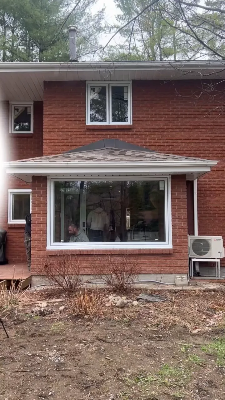 Fenêtre blanche au rez-de-chaussée d’une maison en brique rouge.